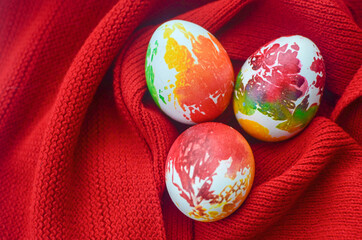 three multi-colored colorful chicken easter eggs lie wrapped in a red knitted scarf