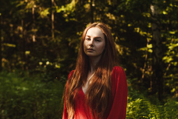 The young woman in red dress in green rainfores. Concept of nature and happy life, adventure. Beautiful light only on face. Fairy tale concept.