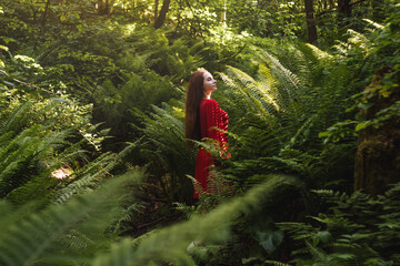 Naklejka na ściany i meble The young woman in red dress in rainforest with fern. Concept of nature and happy life, adventure. Beautiful light and shadow on body. Fairy tale concept.