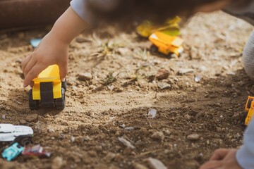 Manos de un chico joven jugando con vehículos de construcción en la arena