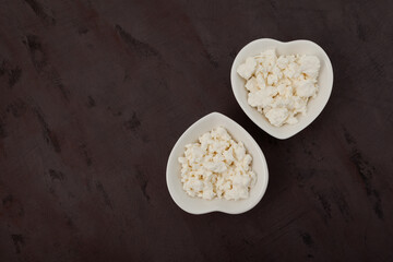 Homemade natural cottage cheese in white bowls in shape of hearts on brown background Natural dairy product. Organic eco healthy food. Top view, copy space