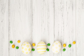 Easter background white wooden table with eggs, yellow and green candies and copy space, bottom border