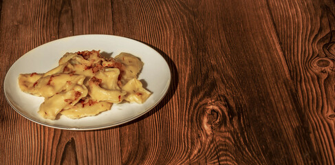 Dumplings with potatoes and fried onions in a white plate on a wooden table. Ukrainian and Russian traditional cuisine. Top view. Copy space. Background. Old New Year.
