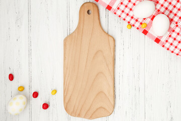 Vertical blank wood cutting board on the white table with Easter eggs. Kitchen template, mockup, copy space