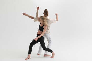 Fototapeta na wymiar Couple of young people practicing contact yoga in studio on white background. А man and a woman lean on each other during psychological therapeutic exercise