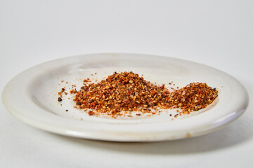 A scattering and a hill of small peppers and spices on a white plate and a white background