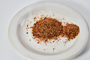 A scattering and a hill of small peppers and spices on a white plate and a white background