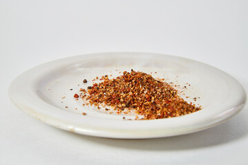 A scattering and a hill of small peppers and spices on a white plate and a white background