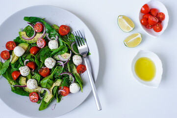 top view of delicious diet salad  with cherry tomatoes, avocado, spinach leaves, Mozzarella and red onion with olive oil dressing served on plate