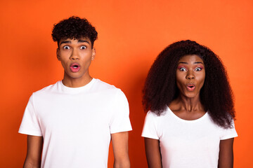 Photo of two impressed dark skin persons open mouth staring camera unexpected news isolated on orange color background