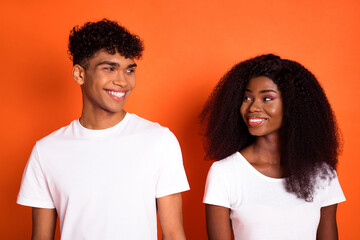 Obraz premium Photo of young happy positive lovely charming afro couple look at each other with love isolated on orange color background