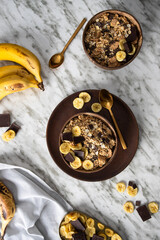  Natural muesli  in coconut bowl with  banana and chocolate on the marble table. Mix of unprocessed whole grains, chia, quinoa, nuts, seeds, fruit for heathy breakfast.