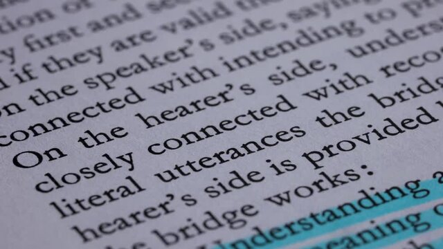 Extremely close up of an English text printed on the open pages of a book. Macro shots of the turning pages, on which the main theses are highlighted in blue and pink markers. Slow motion.