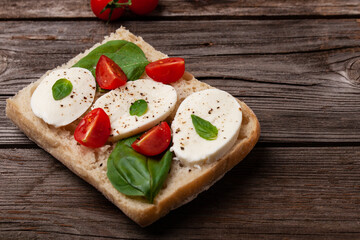 Ciabatta with cherry tomato, basil, mozzarella and spices. Bruschetta with cheese om wooden table. 