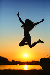 A young athletic girl jumps against the backdrop of the setting sun 