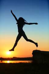 A young athletic girl jumps against the backdrop of the setting sun 