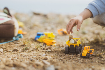 Manos de un chico joven jugando con vehículos de construcción en la arena