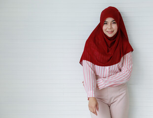 Confident young ethnic woman in Muslim headscarf smiling against white wall