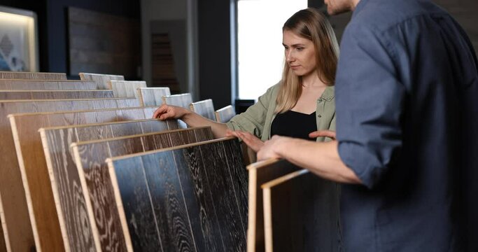 young couple choosing wood texture laminate floor from samples for home improvements in interior design store