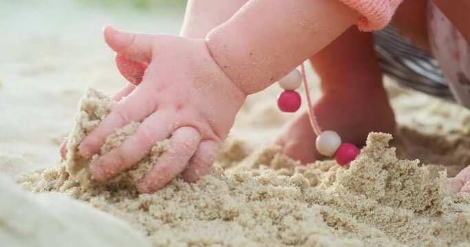 Sand games. Baby plays with sand on the beach, close up shot with hands in the frame