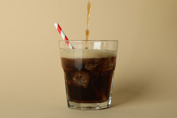 Cola is poured into a glass on beige background