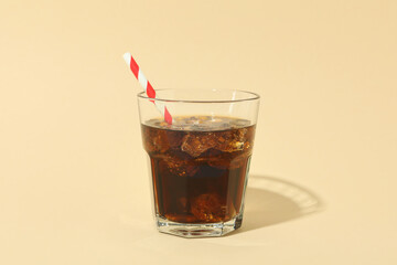 Glass of cola with ice cubes and straw on beige background