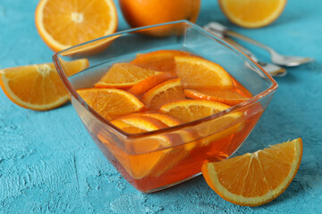 Bowl of orange jelly with orange slices on blue textured background