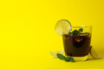 Glass of Cuba Libre on yellow background, space for text