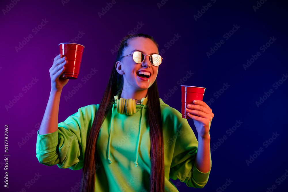 Poster Photo of cheerful happy young woman look empty space hold red plastic cups isolated on gradient background