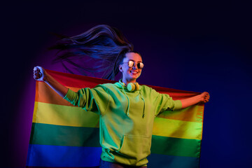 Photo of charming happy proud young woman hold rainbow flag lgbtq fly hair isolated on neon...
