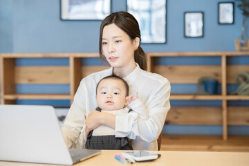 赤ちゃんを抱えてノートパソコンを操作する女性