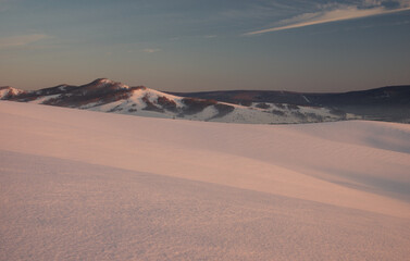 Fototapeta na wymiar Winter sunset snow field on top of mountain slope on the background of hills under colorful sky