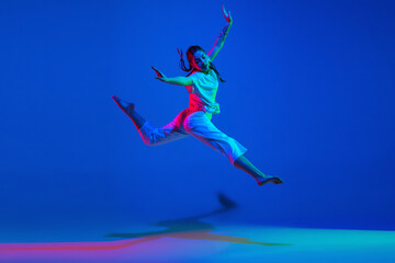 Young girl dancing hip-hop in white attire on colorful background in neon light
