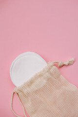 Reusable cotton pads for facial care in eco bag on pink background