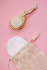 Reusable cotton pads for facial care in an eco bag and a wooden brush on a pink background