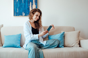 Happy casual beautiful woman is talking on a phone sitting on a sofa at home.