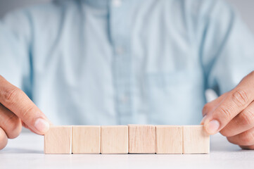 Businessman wearing a blue shirt, arranging the empty wooden blocks with his hands. Which is placed on a white wooden table. Business strategy and action plan. Copy space.