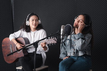 Fototapeta na wymiar Asian female singer with a passion for music and microphone. While playing her guitar in a professional studio. Music concept, sound recording concept.
