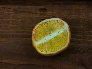 Ugly food trend. Spoiled yellow lemon half with red mold close up on wooden background. Moldy...