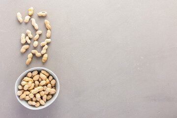 Legumes in bowl and scattered in the background, peanuts in a plate on a gray background, top view, copy space