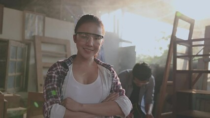 Portrait of asian woman carpenter standing smiling and arms crossed with wearing safety eyes goggle in furniture factory. Happy female young attractive carpenter posing and look on camera in workplace