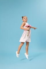 very excited happy little girl with bouquet of roses jumps on blue background. mothers day