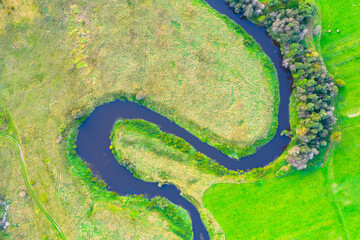Winding river on a plain with trees and meadows on the shore, aerial view.