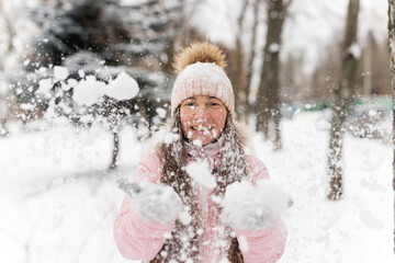 Portrait of young woman playing and throwing snow