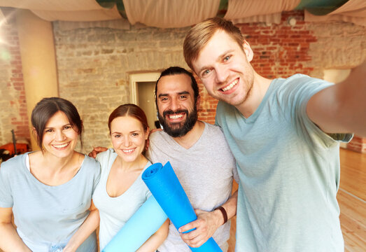 fitness, sport and healthy lifestyle concept - group of happy people with mats at yoga studio or gym taking selfie
