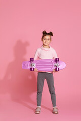 little child girl with pink skateboard in casual clothes on pink background.