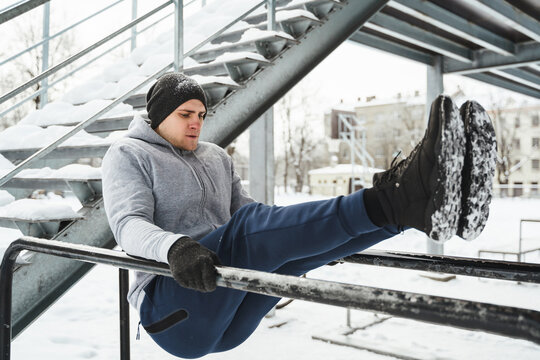 Man during calisthenics workout on a parallel bars during snowy winter day