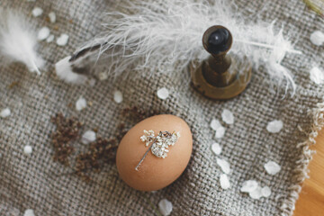 Easter egg decorated with dry flower petals on background of rustic linen napkin,candle and feather