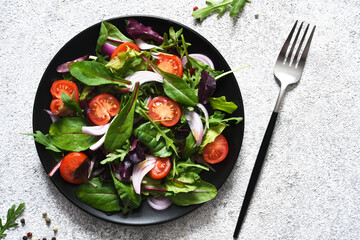 Mix salad with tomatoes, onions and olive oil in a black plate. Detox menu. The keto diet.