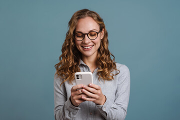 Happy girl in eyeglasses smiling while using mobile phone